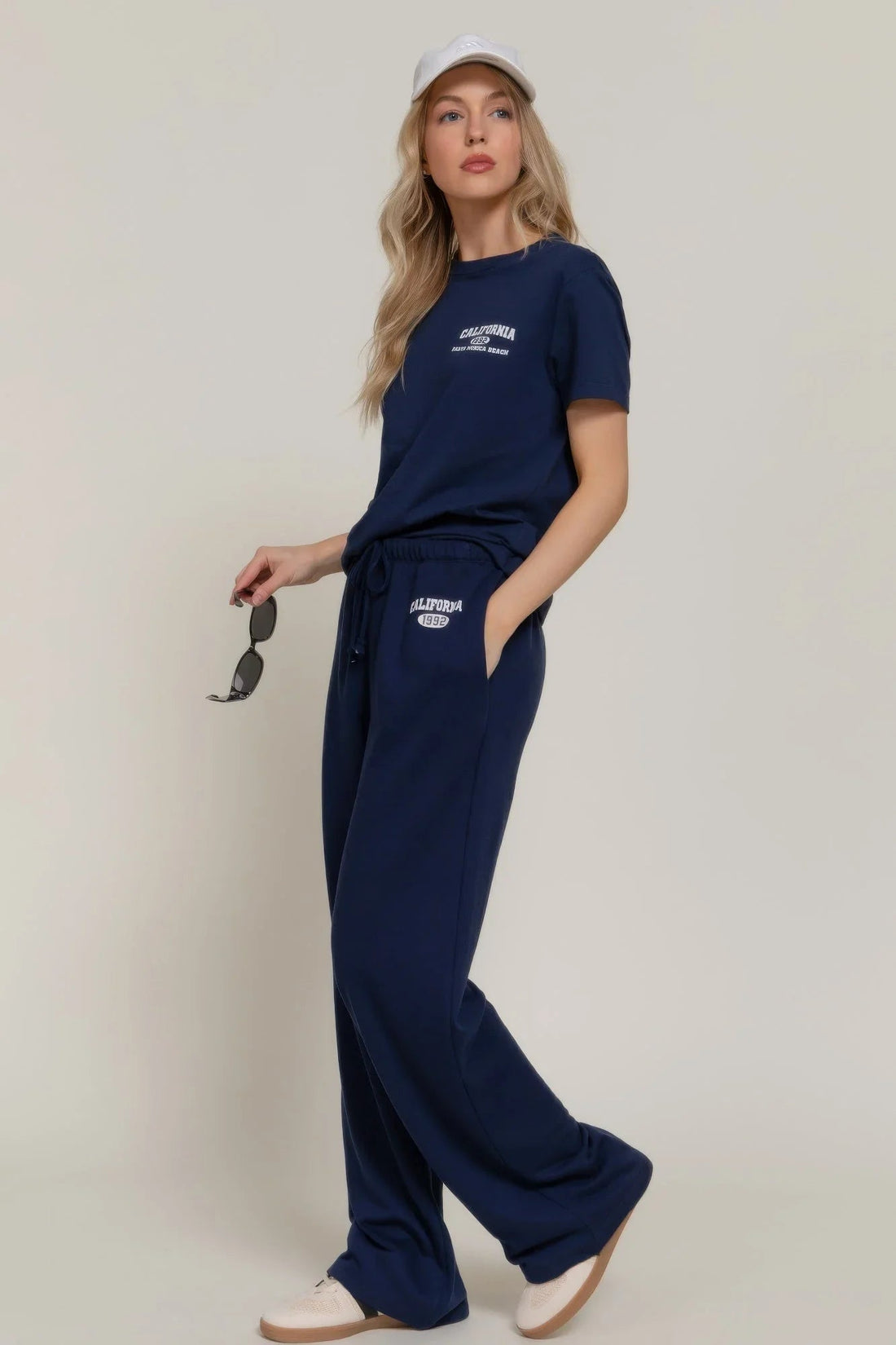Woman modeling navy IVORYNN sweatpants and t-shirt set with cap, casual fashion style