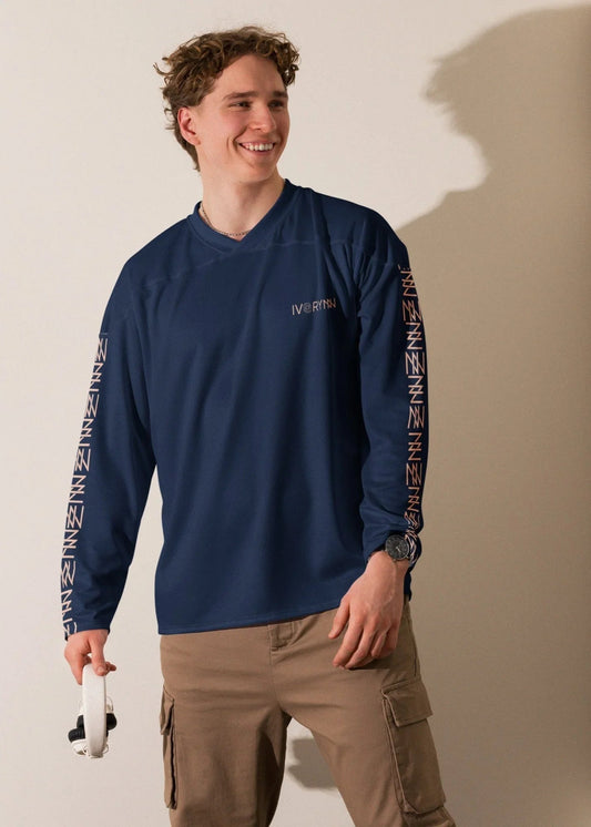 Smiling man wearing IVORYNN navy blue long sleeve sportswear top with logo, khaki pants, holding headphones
