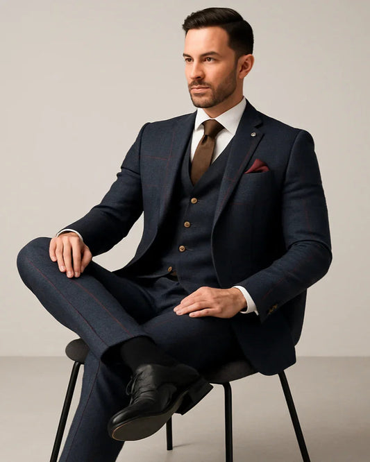 Man in a tailored navy suit with brown tie and dress shoes, sitting on a chair, stylish menswear Ivorynn