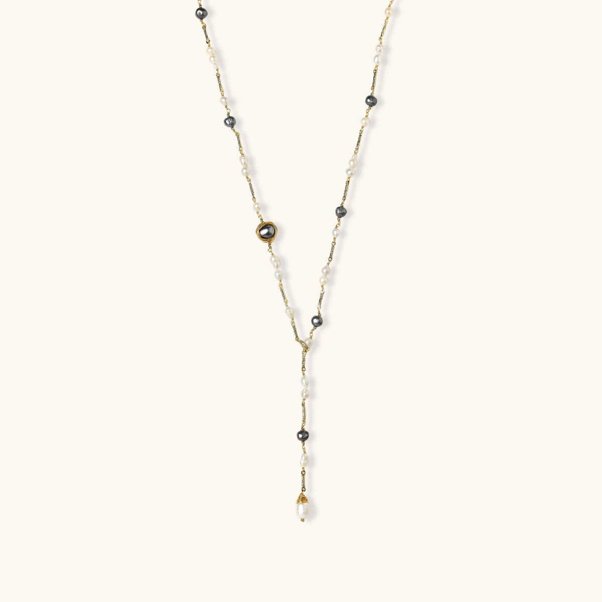 Y-shaped gold-plated necklace with white and gray freshwater pearls on cream background, showing adjustable drop design.
