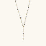 Y-shaped gold-plated necklace with white and gray freshwater pearls on cream background, showing adjustable drop design.