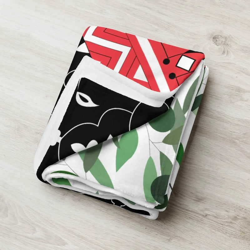 Folded ivory throw blanket with bold red, black, and green floral and geometric patterns on wood surface