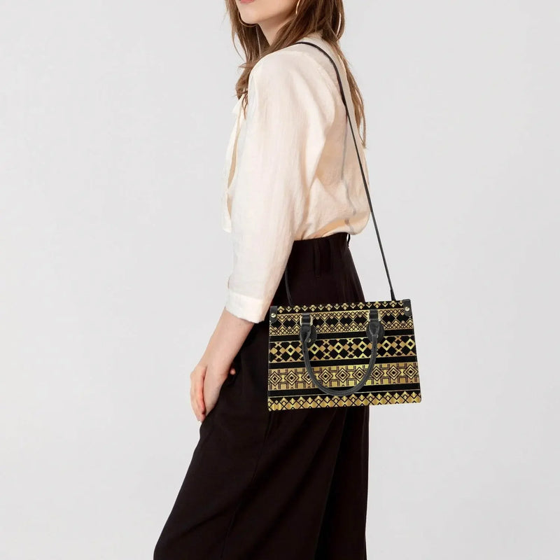 Woman wearing modern ivory blouse and black pants, carrying a black and gold patterned tote bag with long strap from Ivorynn fashion collection.