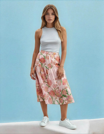 Woman in a sleeveless grey top and ivory floral ruffle skirt from Ivorynn, standing against a blue background.