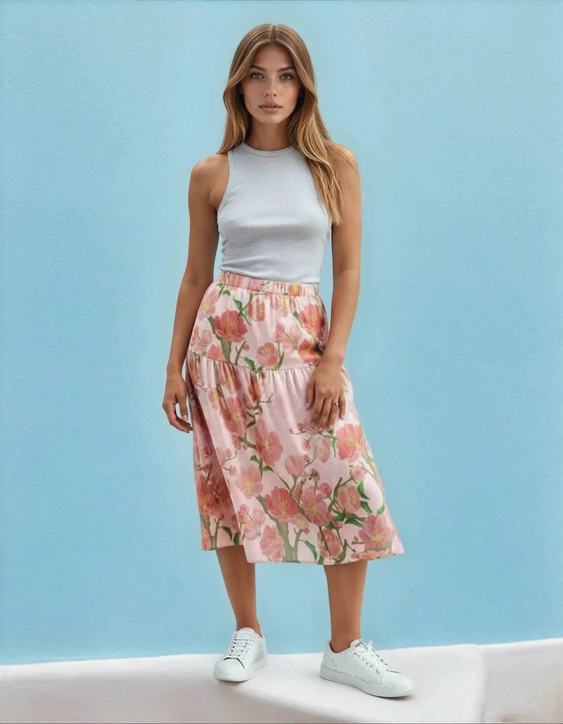 Woman in a sleeveless grey top and ivory floral ruffle skirt from Ivorynn, standing against a blue background.