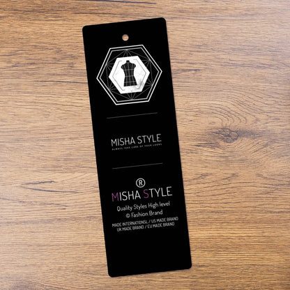 Black Misha Style clothing tag with geometric dress icon on wood surface, fashion brand label.