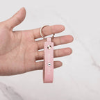 Hand holding a pink leather keychain with gold ring and 'MISHA STYLE' text, marble background