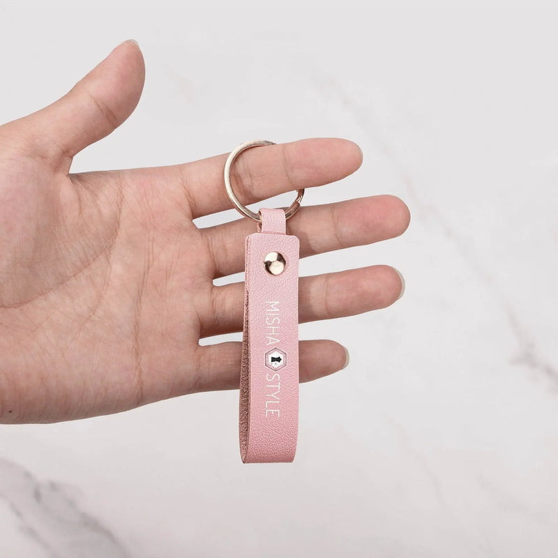 Hand holding a pink leather keychain with gold ring and 'MISHA STYLE' text, marble background