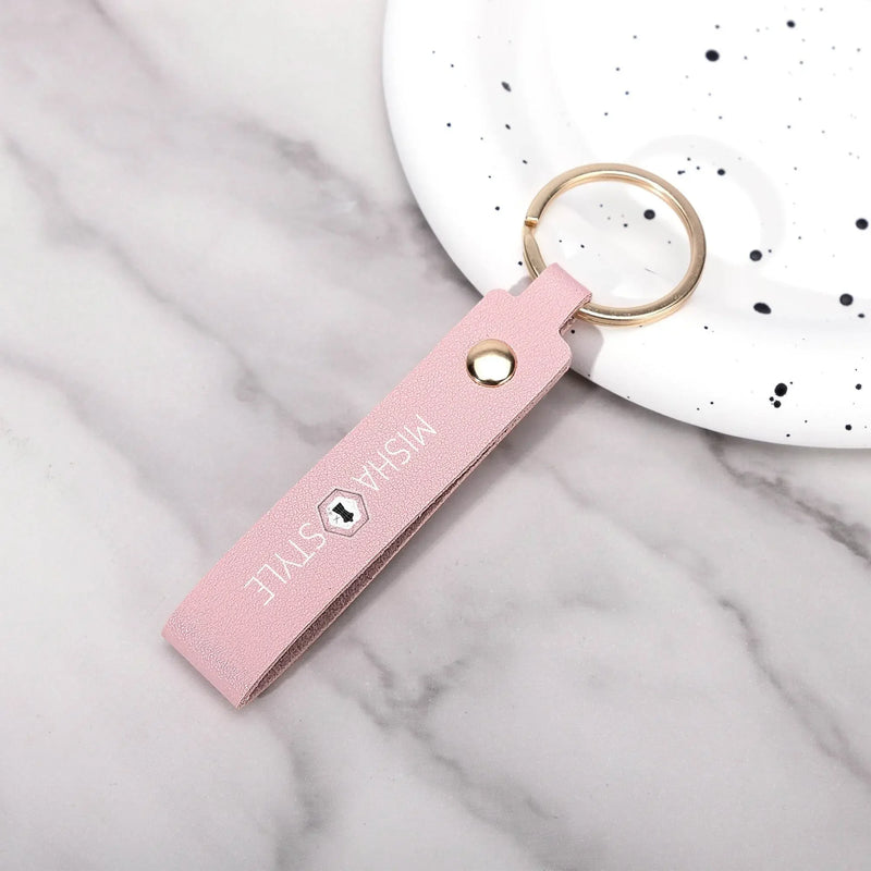 Pink leather keychain with gold ring and 'MISHA STYLE' text, on marble surface near white speckled dish