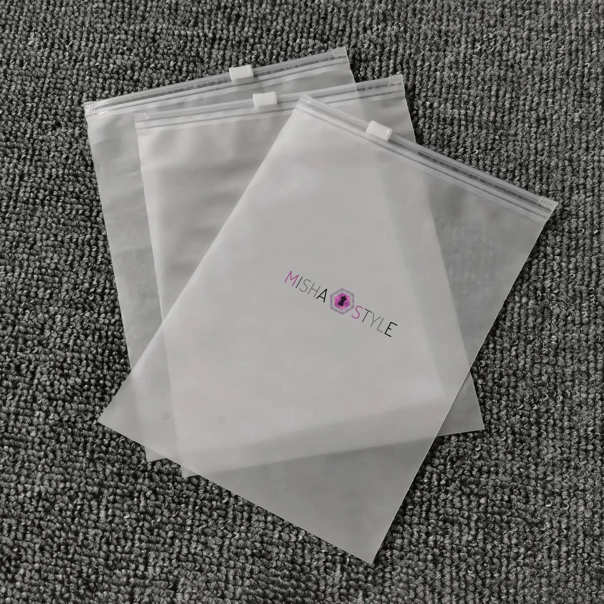 Three clear MISHA STYLE zipper bags on textured gray carpet