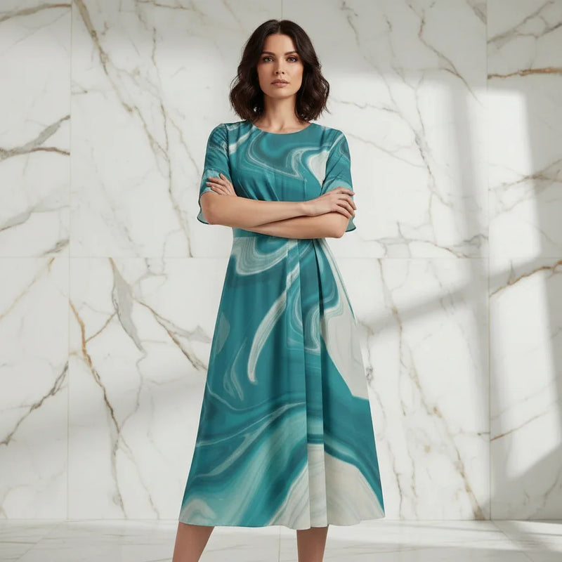 Confident woman in a stylish teal marble-print dress, arms crossed, standing in modern marble room