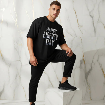 Athletic man in black 'Happy Liberty Day' t-shirt and black pants posing on marble pedestal, Ivorynn mens fashion