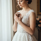 Bride in lace wedding dress holding ring box near window, Ivorynn bridal fashion