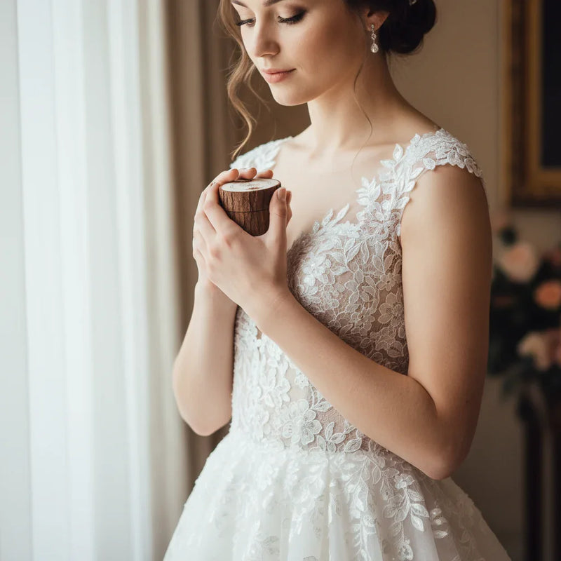 Bride in lace wedding dress holding ring box near window, Ivorynn bridal fashion
