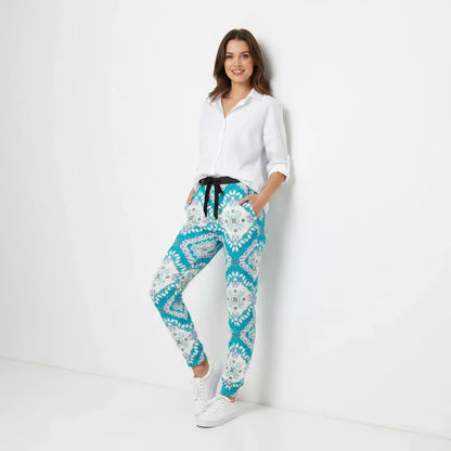 Woman in a white shirt and patterned blue pants, leaning against a white wall, stylish casual fashion from Ivorynn.
