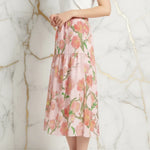 Woman in elegant floral midi skirt by Ivorynn, side pose, marble background.