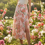 Woman in pink floral slit skirt standing in blooming garden, stylish spring fashion at Ivorynn