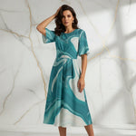 Woman in teal marble print midi dress posing against marble wall, stylish women's fashion at Ivorynn