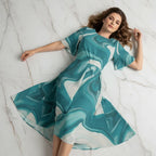 Woman in a flowing teal and white patterned dress on a marble floor, Ivorynn fashion