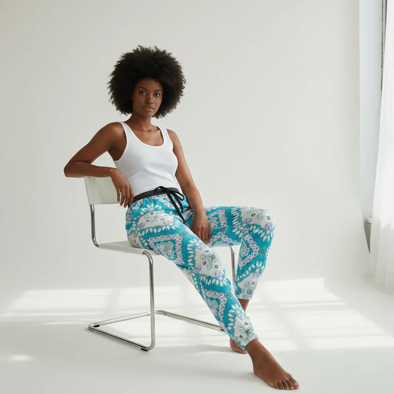 Woman in white tank top and patterned blue pants sitting by window, Ivorynn fashion lifestyle