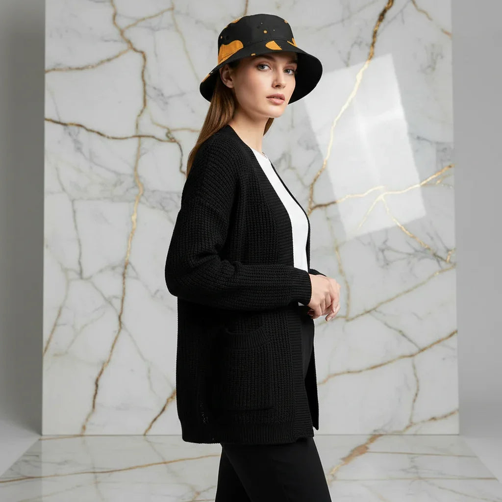 Woman in black knit cardigan, white top, and bucket hat posing in a modern marble setting