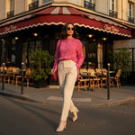 Woman in a pink floral shirt and cream trousers walking stylishly outside a Parisian café