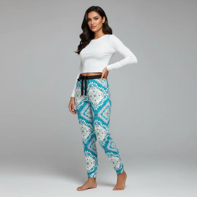 Woman modeling Ivorynn women's fashion, wearing a white long sleeve top and patterned jogger pants, in a studio with a gray backdrop.