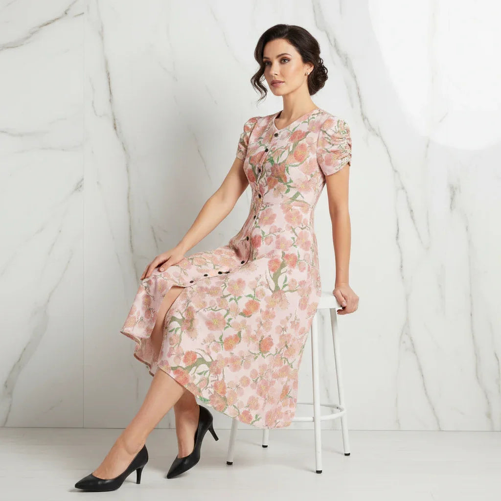 Woman in a floral midi dress and black heels seated on a stool, stylish fashion at Ivorynn