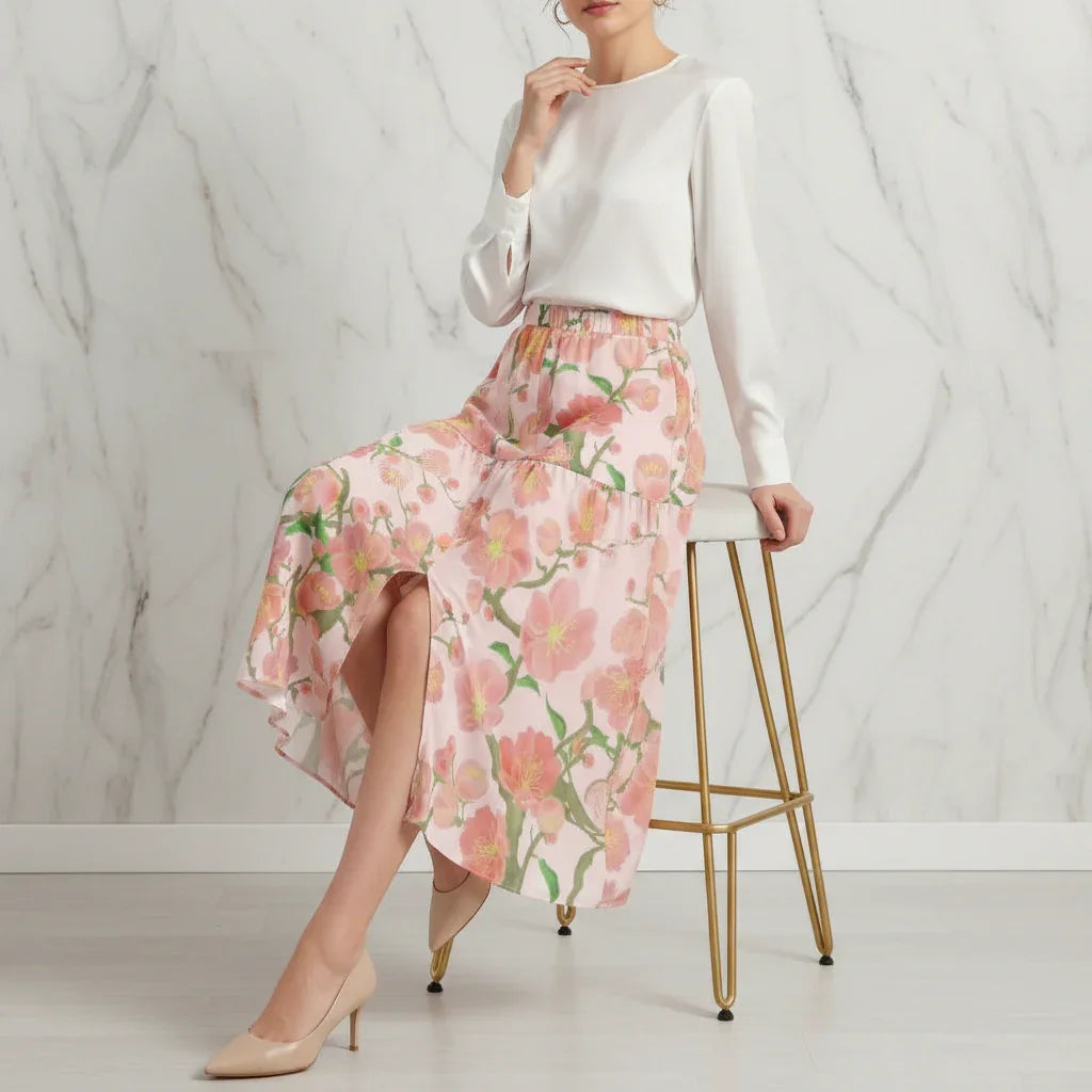 Woman in stylish ivory blouse and pink floral skirt seated on modern stool, Ivorynn fashion