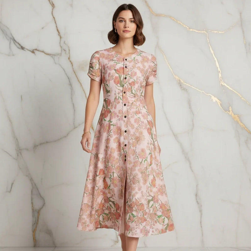 Woman wearing a floral pink dress posing against a marble wall, Ivorynn fashion apparel