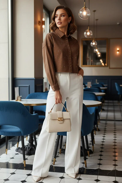 Woman in brown denim shirt with white pants, full body standing in café
