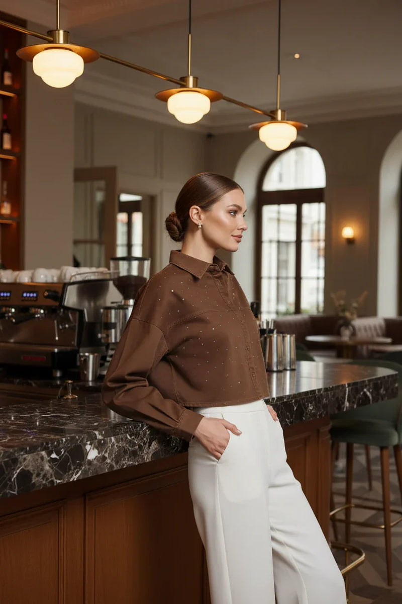 Woman in brown denim shirt with white pants, side view at café bar
