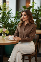 Woman in brown denim shirt with white pants, three-quarter view at café table