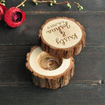 Personalized rustic wooden ring box with engraved names, two rings inside, on dark wood table
